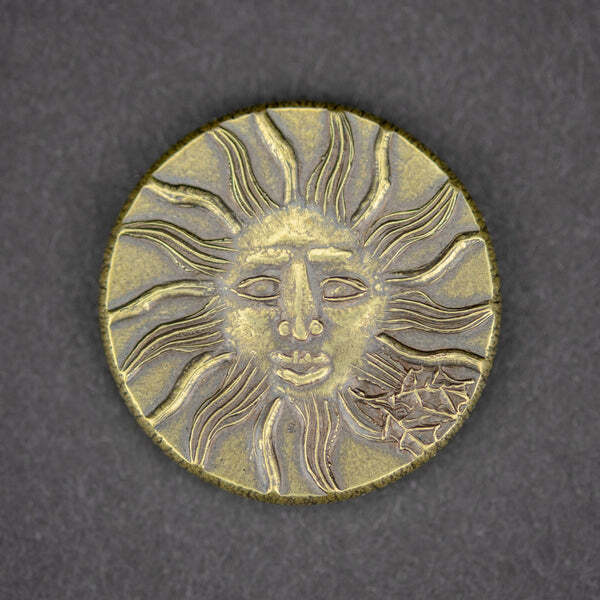 A gold-looking coin eith sun personification (face), against grey fabric backdrop.